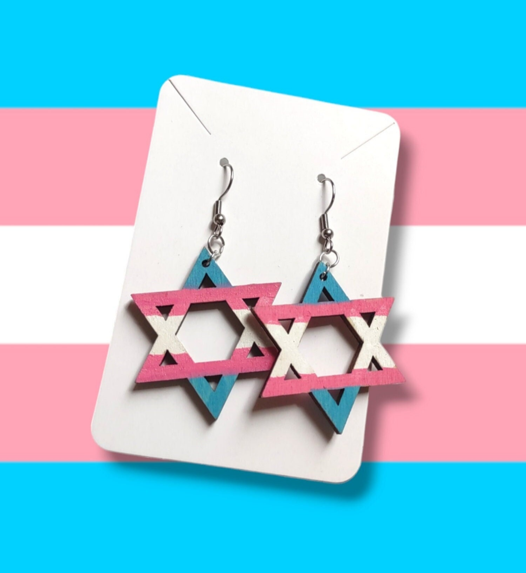 Star-shaped earrings on a display card with a trans pride flag background