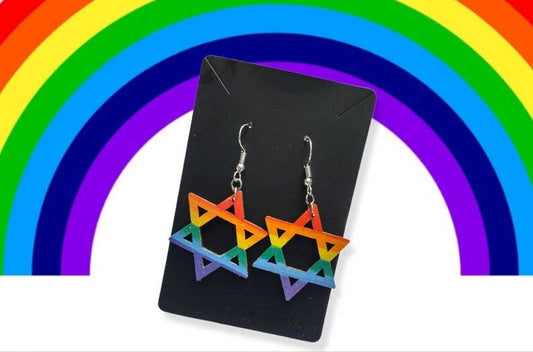 Rainbow-colored star-shaped earrings on a black card with a rainbow background